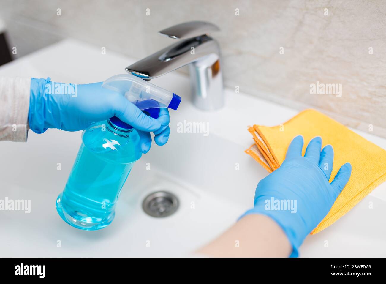 Female hands wearing rubber gloves holding microfiber cloth and spray