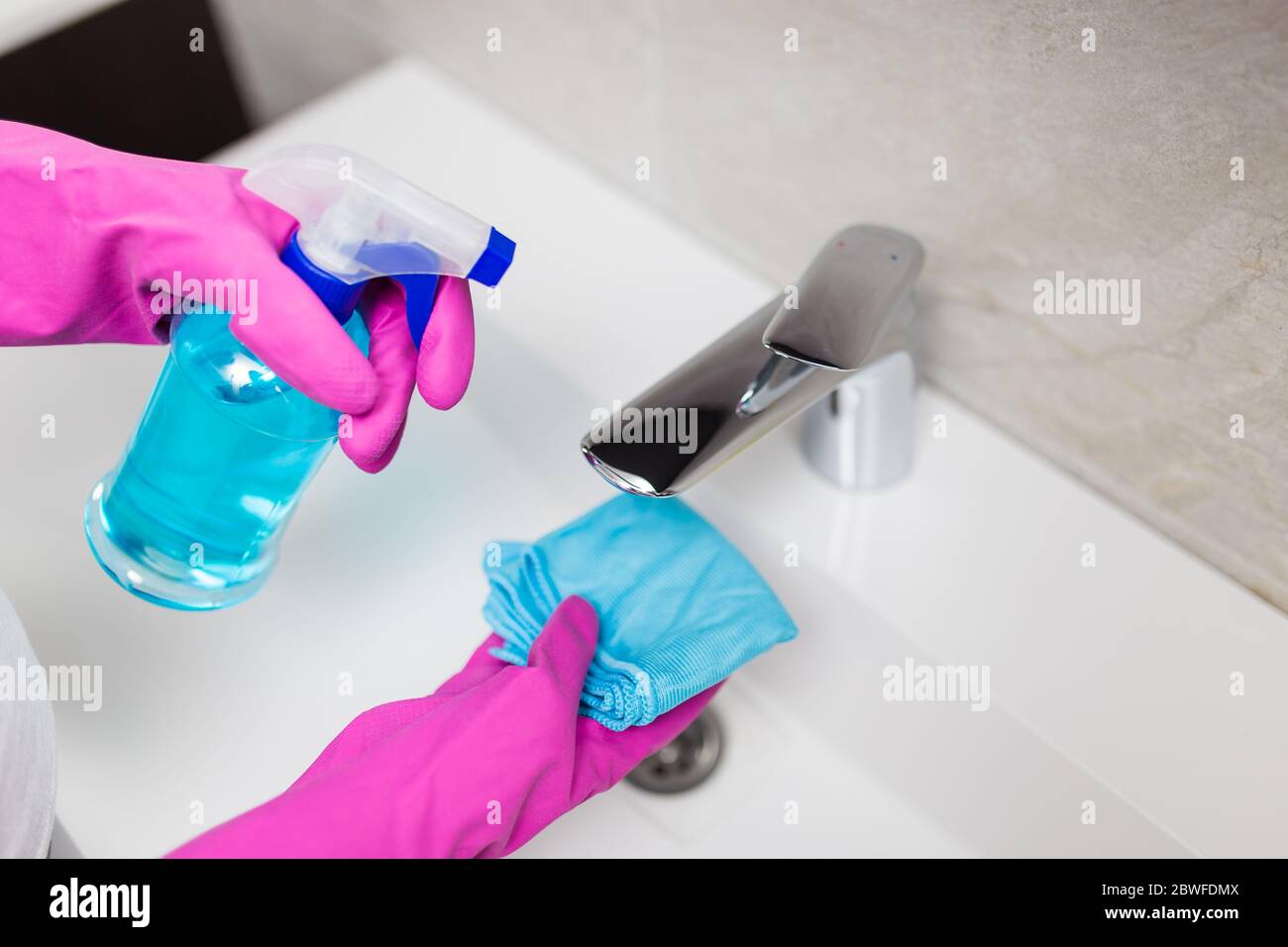 Female hands wearing rubber gloves holding microfiber cloth and spray