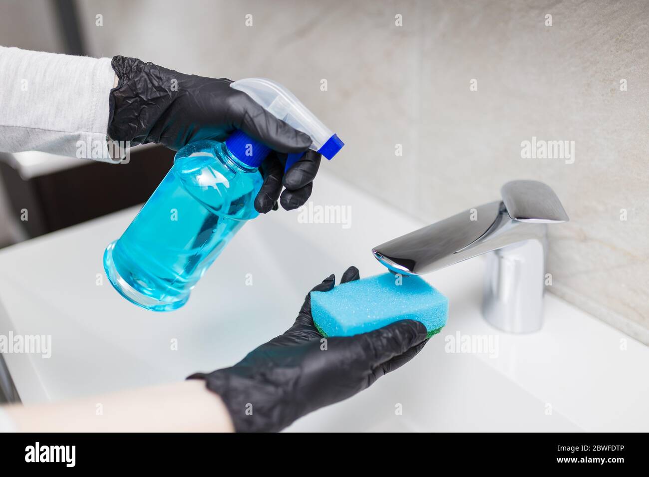 Female hands cleaning sink tap faucet in bathroom to disinfect from virus or bacteria and clean