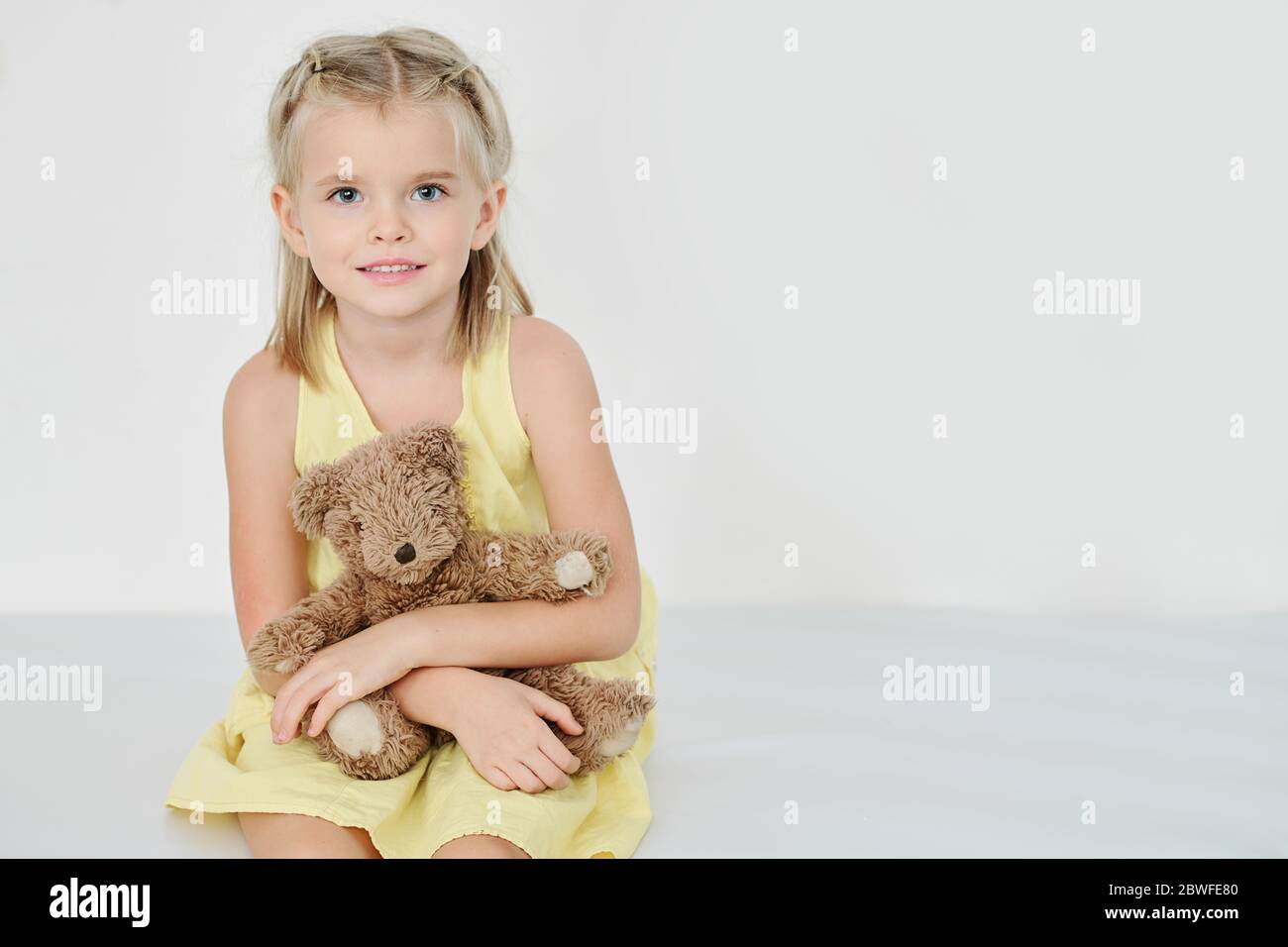 Portrait of smiling little girl with teddy bear sitting on the floor ...