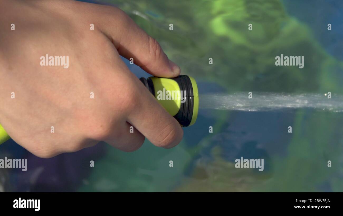 teenager hand filling Inflatable pool with water from hose in garden in