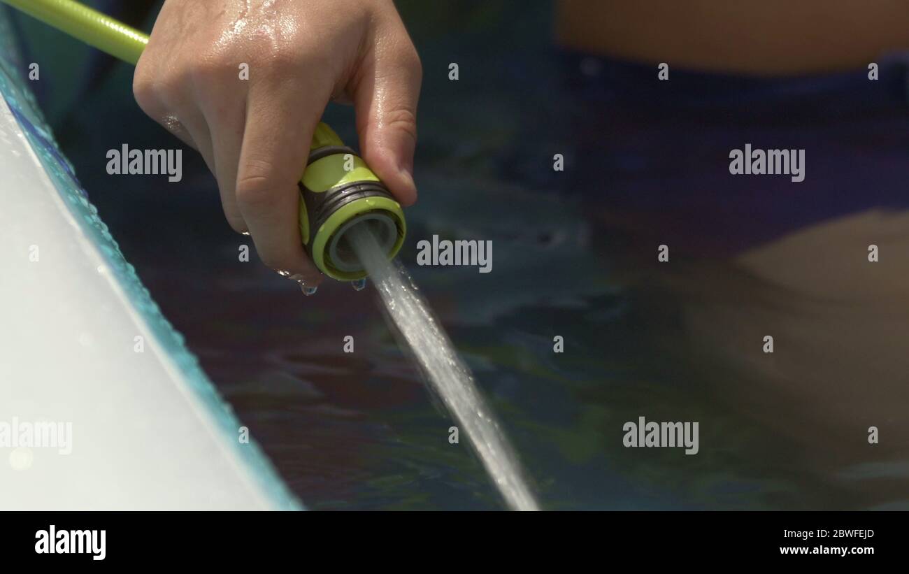 teenager hand filling Inflatable pool with water from hose in garden in