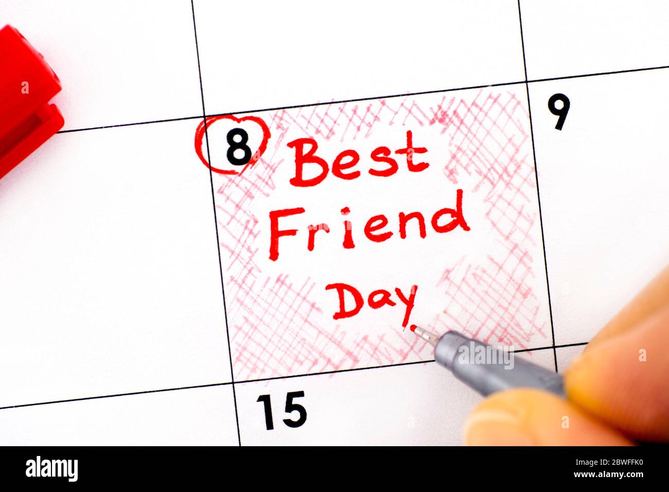 Woman fingers with pen writing reminder Best Friend Day in calendar
