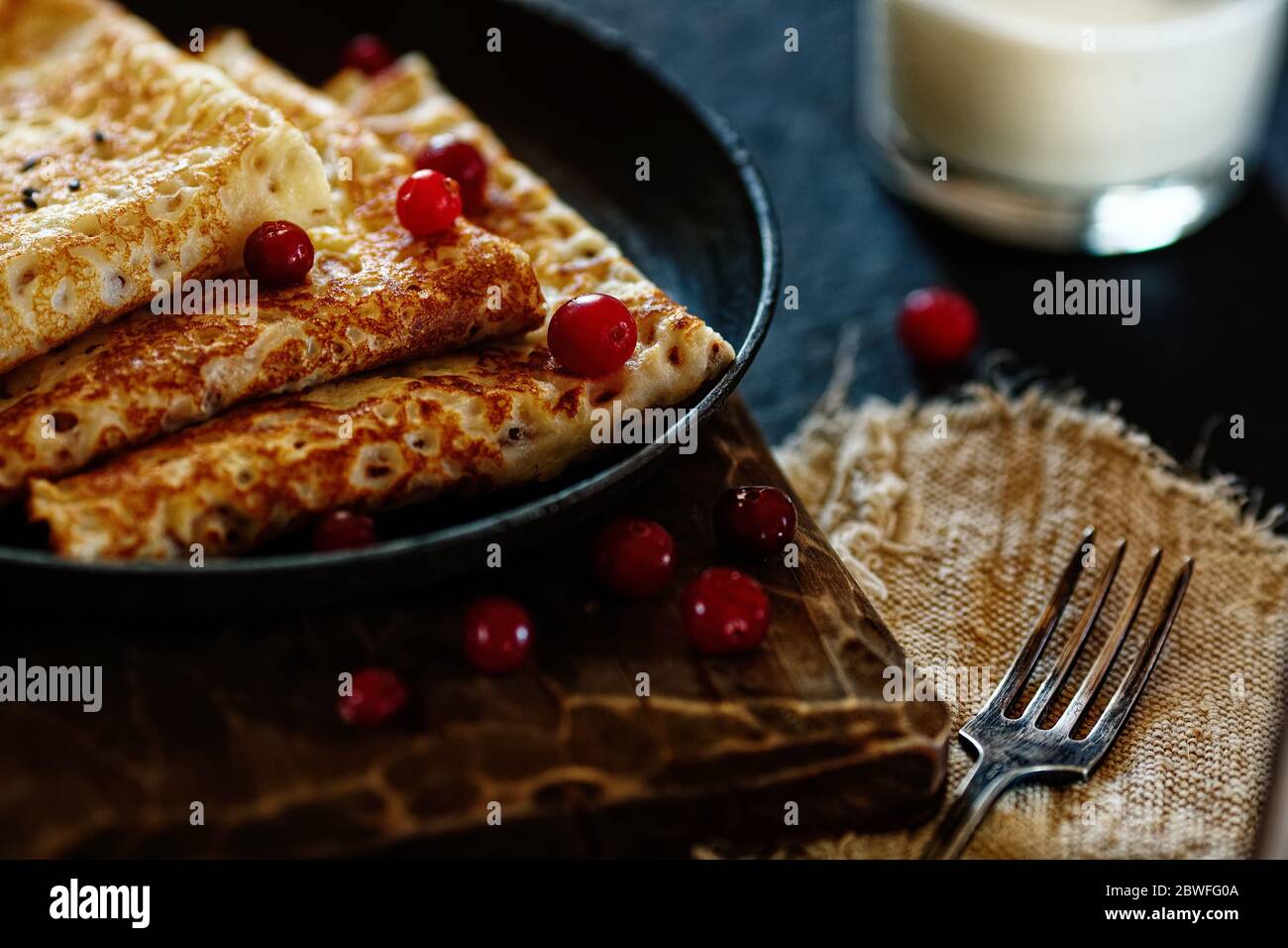 Delicious home-cooked food. Pancakes in a frying pan with cranberry berries and milk. National Russian cuisine. Rustic style Stock Photo