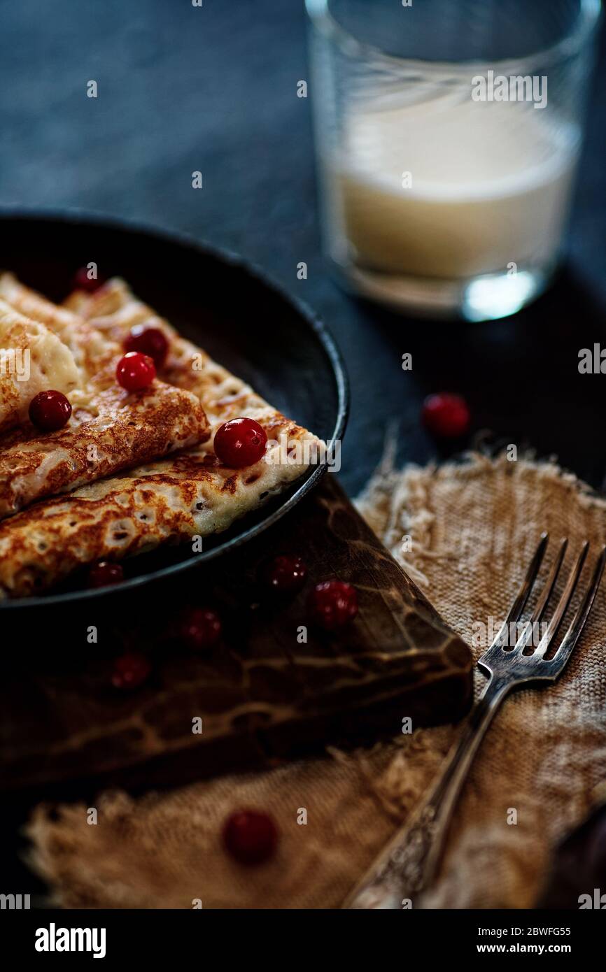 Delicious home-cooked food. Pancakes in a frying pan with cranberry berries and milk. National Russian cuisine. Rustic style Stock Photo