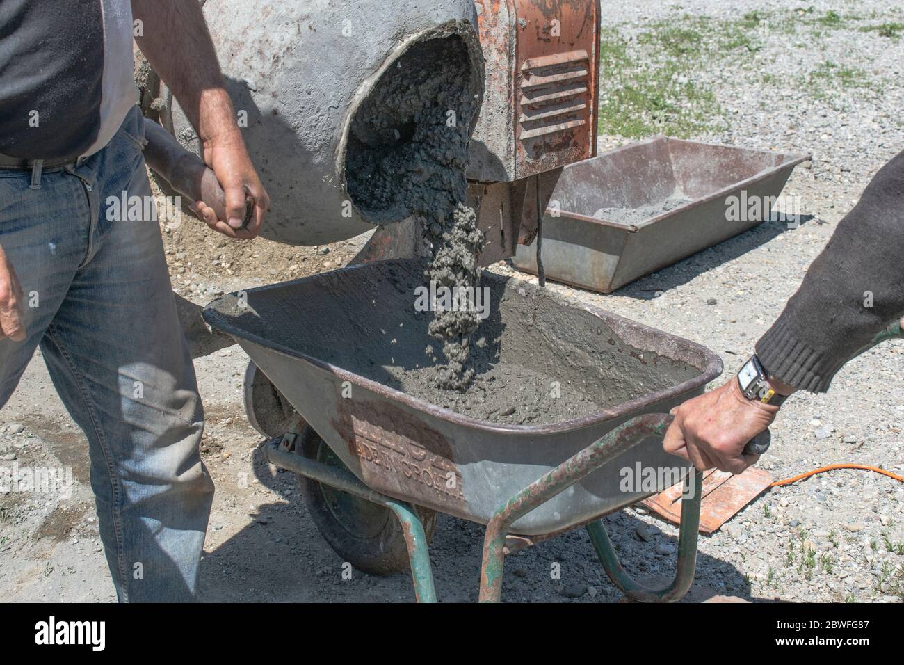 Workers pouring concrete from portable concrete/mortar mixer into wheelbarrow Stock Photo