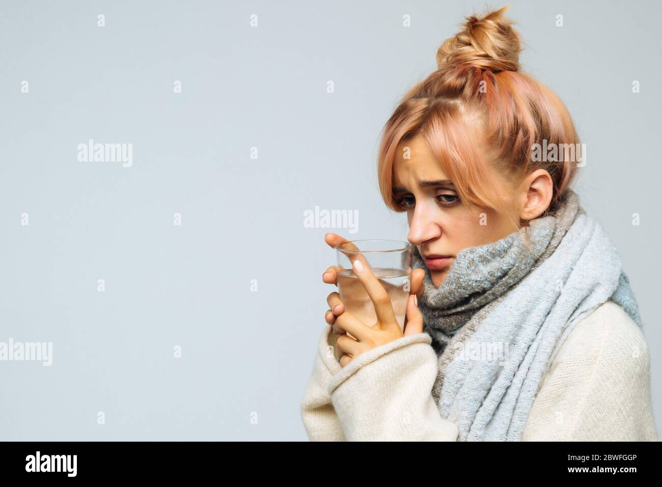 Sickness cute young woman with strawberry blonde hair, warm scarf holding glass of water, feeling the first symptoms of illness. Health problems Stock Photo