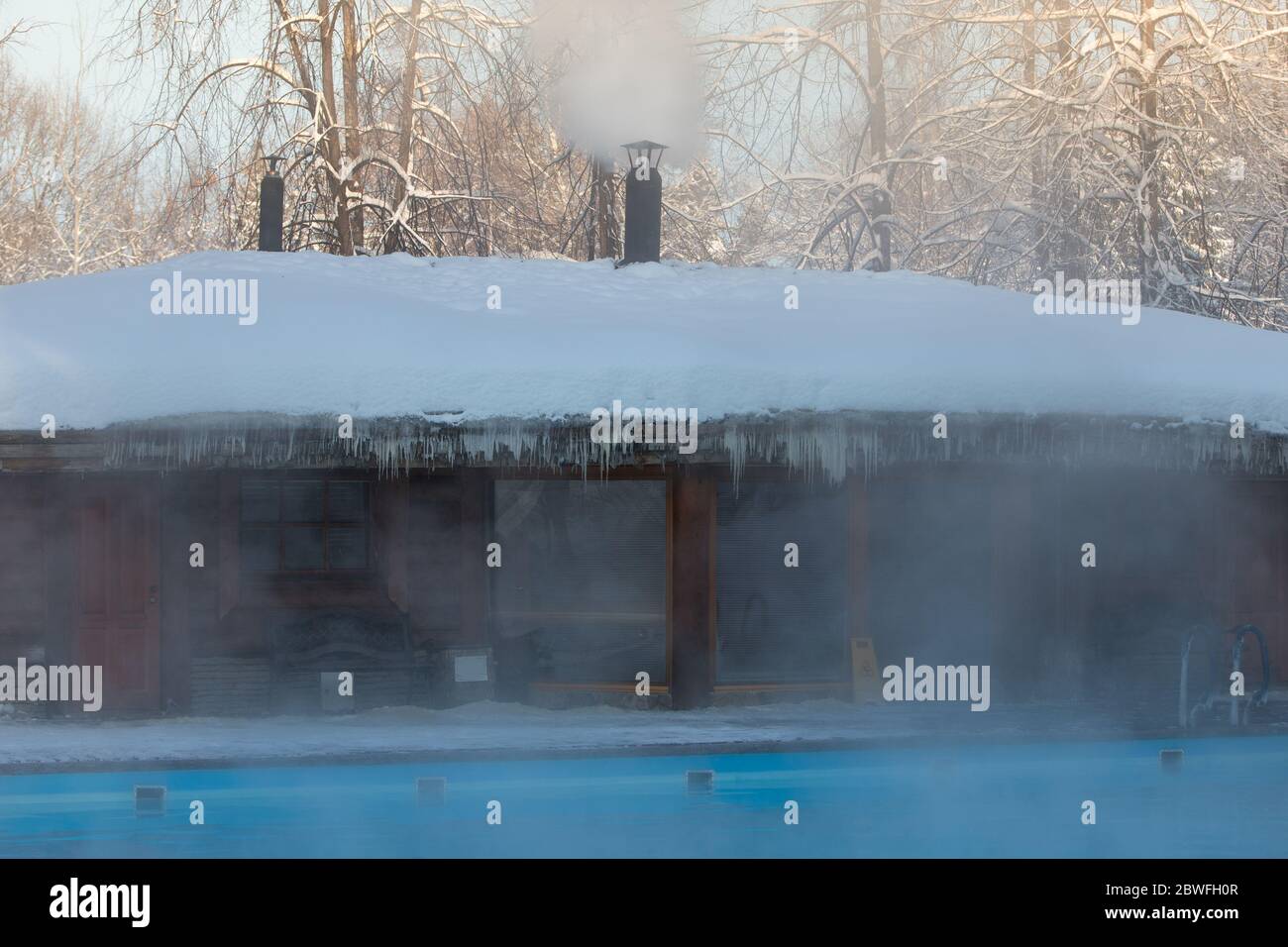 Warm swimming pool with blue water and wooden Russian bath in frosty weather, outdoor Stock Photo