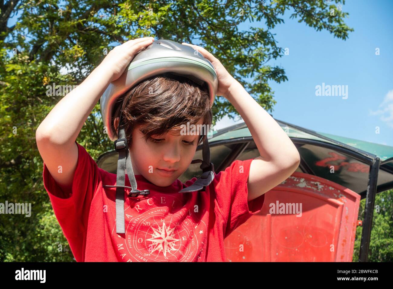 A young child putting on a bicycle helmet in the park, fastens a buckle on a chin strap. Stock Photo