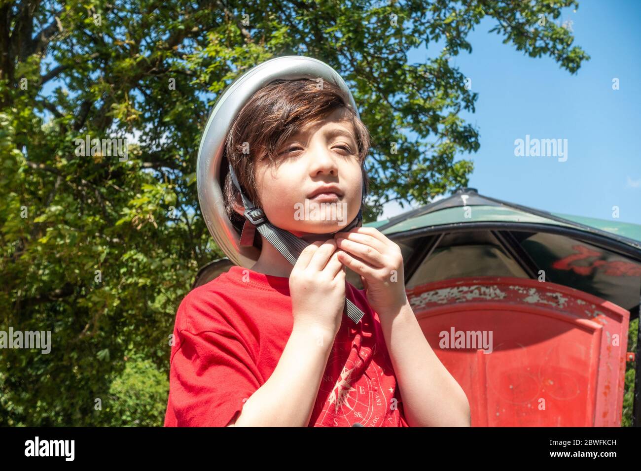 A young child putting on a bicycle helmet in the park, fastens a buckle on a chin strap. Stock Photo