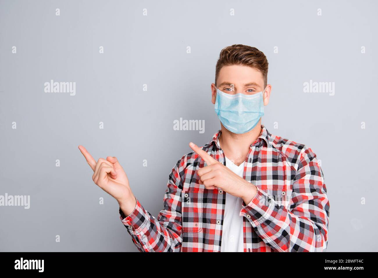 Cheerful young man pointing away wear medical safety mask on face showing data, stop pandemic corona virus prevention protection concept 2020 covid19 Stock Photo