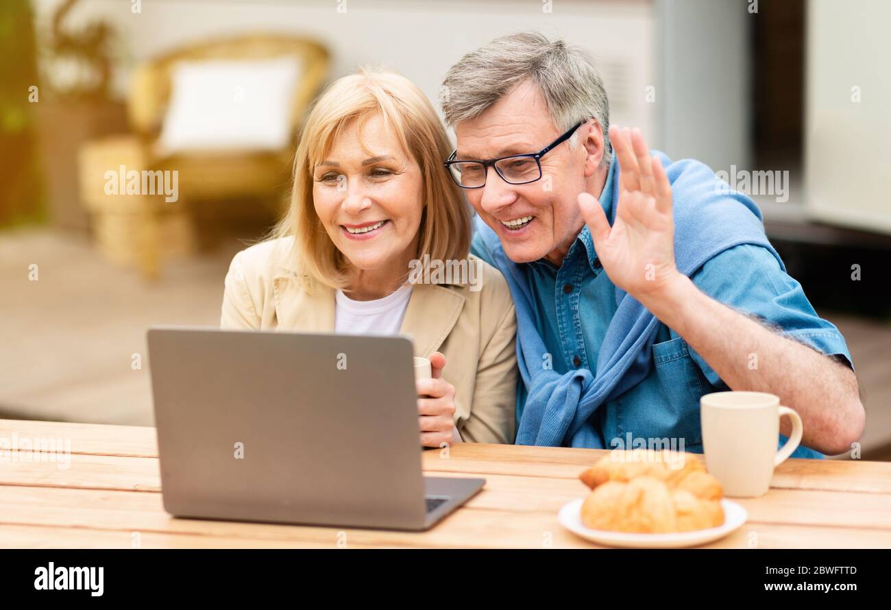 Friendly mature couple chatting online via laptop near RV at campsite Stock Photo