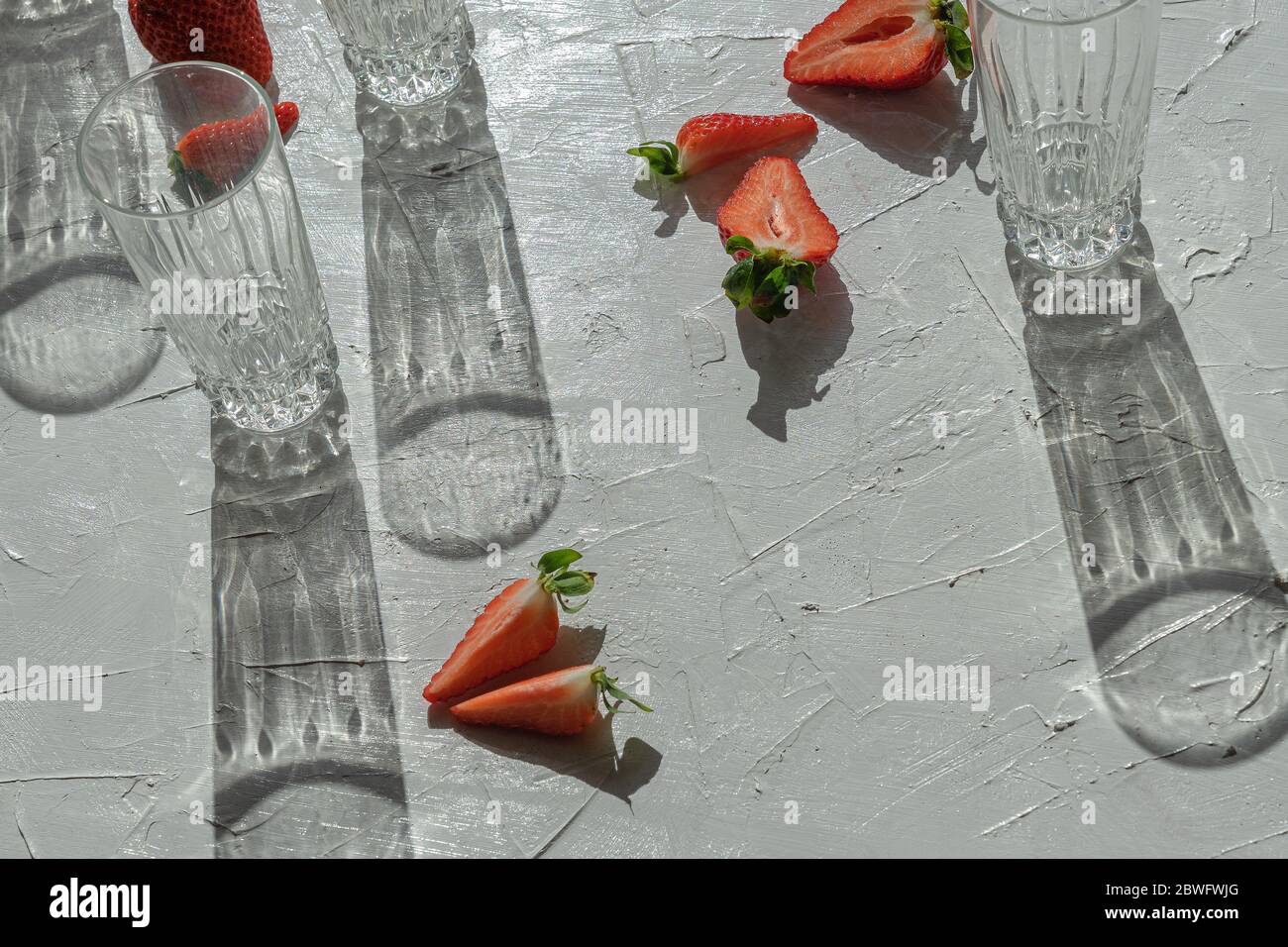 Pieces of fresh juicy chopped strawberries and empty glasses of juice with spectacular transparent shadows in front of bright sunlight Stock Photo