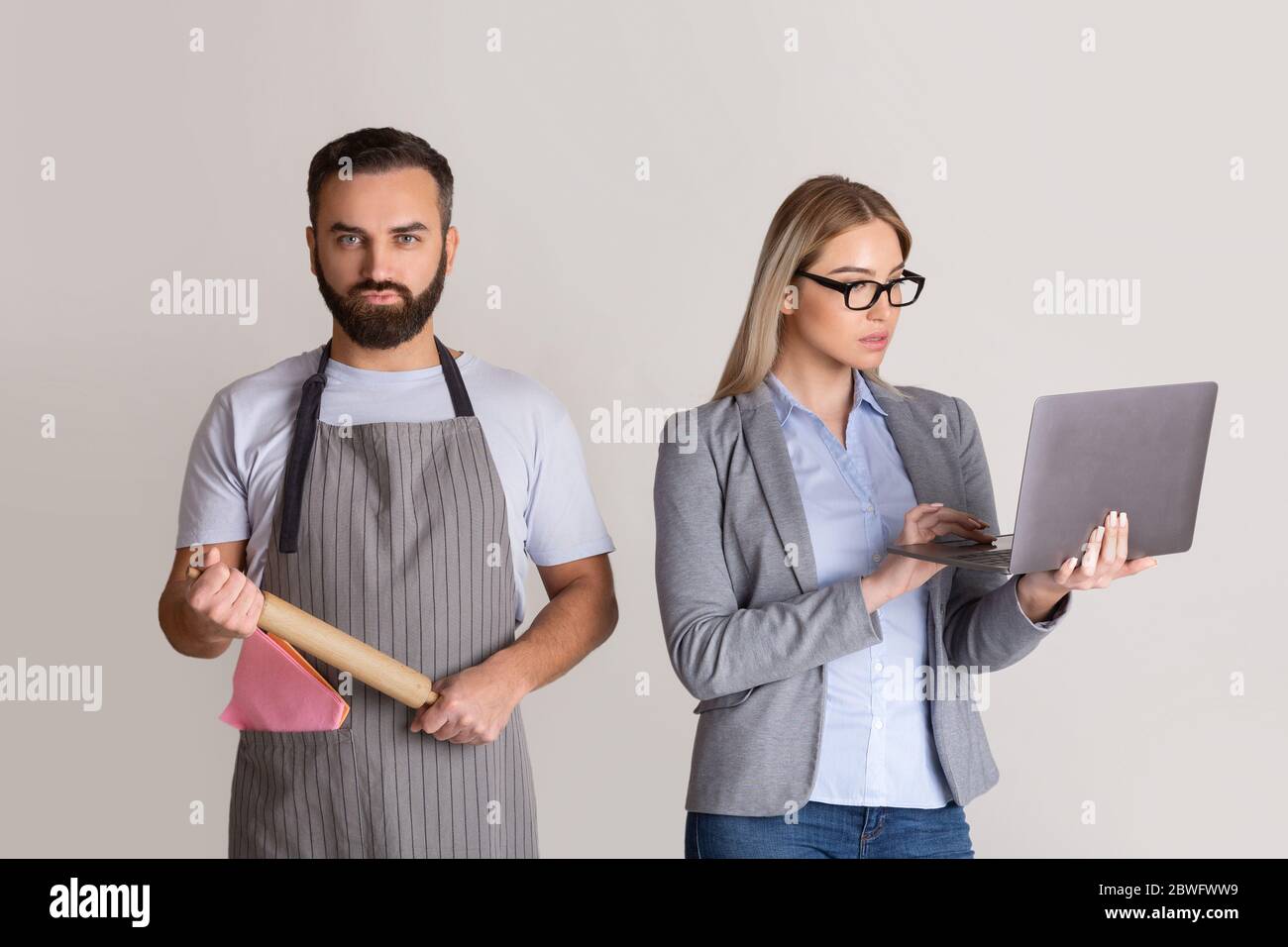 Wife in formal suit with glasses and with laptop in hands, man in apron