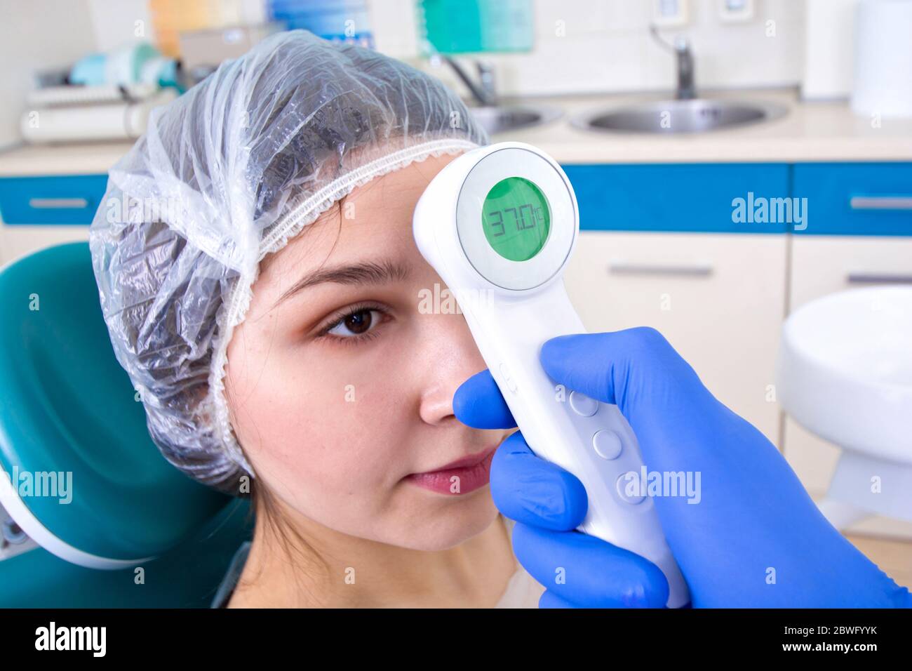 Doctor in protective suit uniform checking temperature of young female patient. Coronavirus outbreak. Covid-19 concept. Stock Photo