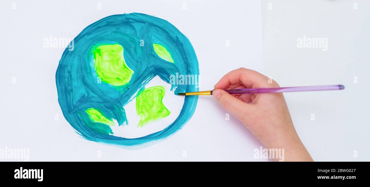 Top view of little girl is drawing earth by watercolors on white paper. Earth Day concept. Stock Photo
