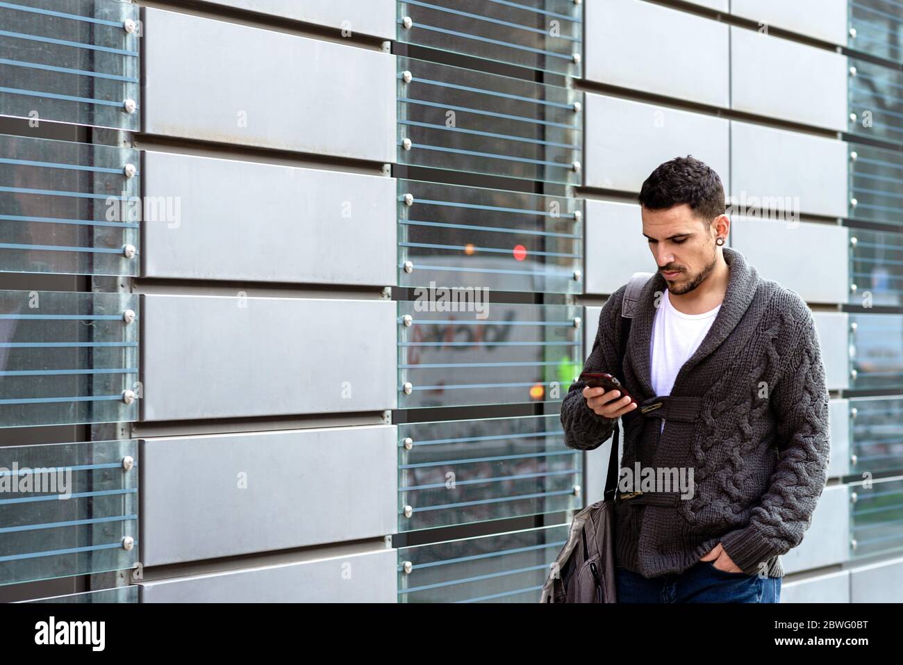Young bearded man walking in the street while using a smartphone Stock Photo