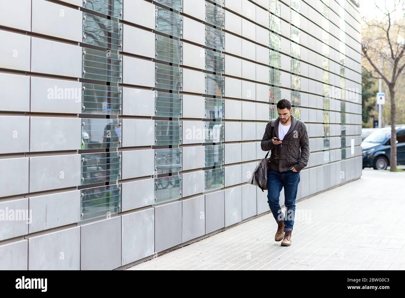 Young bearded man walking in the street while using a smartphone Stock Photo