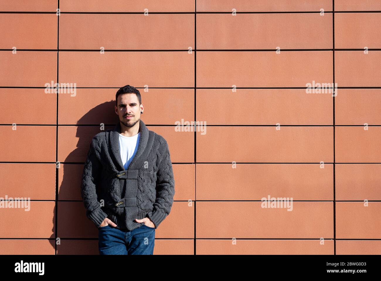 Front view of a fashionable young man standing against orange wall ...