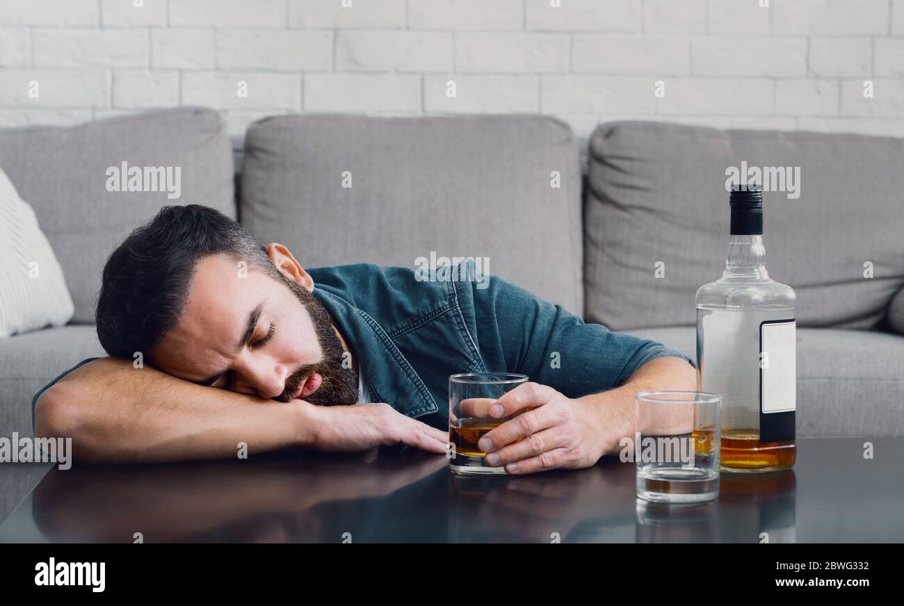 Alcohol addiction. Drunk man sleeping leaning on table with bottle and glass Stock Photo