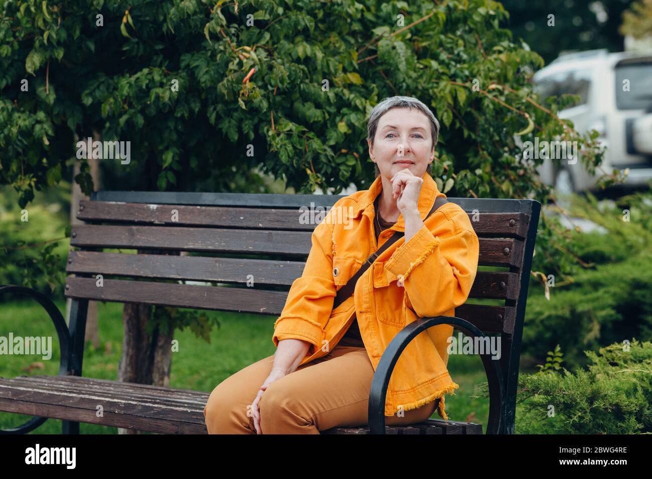 Happy stylish stylish fashionable senior woman sitting on a bench in the city streets. anti aging concept Stock Photo