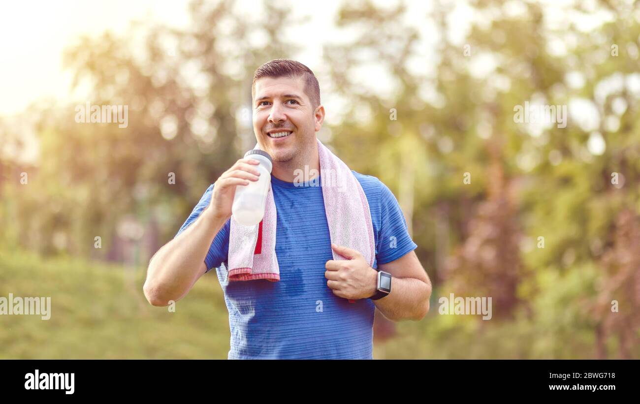 Sweaty mature jogger man drinking water after jogging Stock Photo