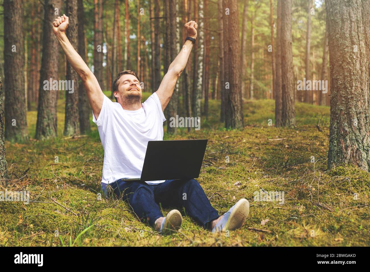 remote job - man with laptop enjoying working outdoors. hands raised Stock Photo