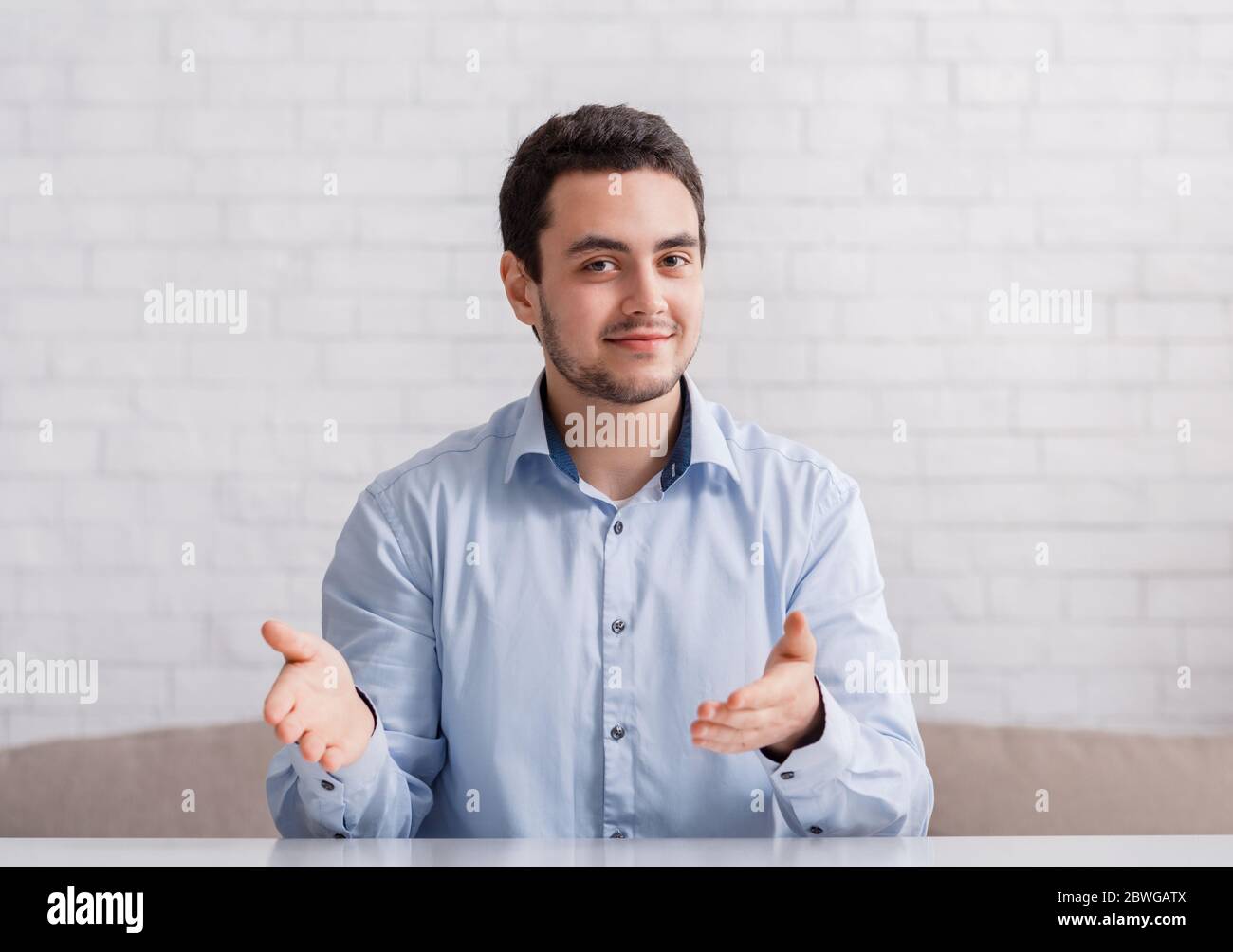 Friendly man point hands to empty space, sitting on couch in interior Stock Photo