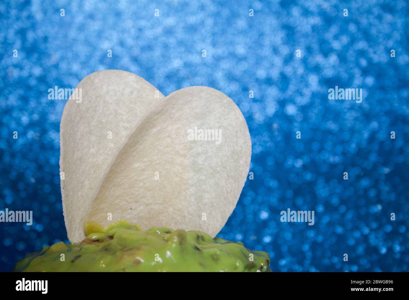 Potato chips with guacamole sauce with green avocado on a blue background. Stock Photo