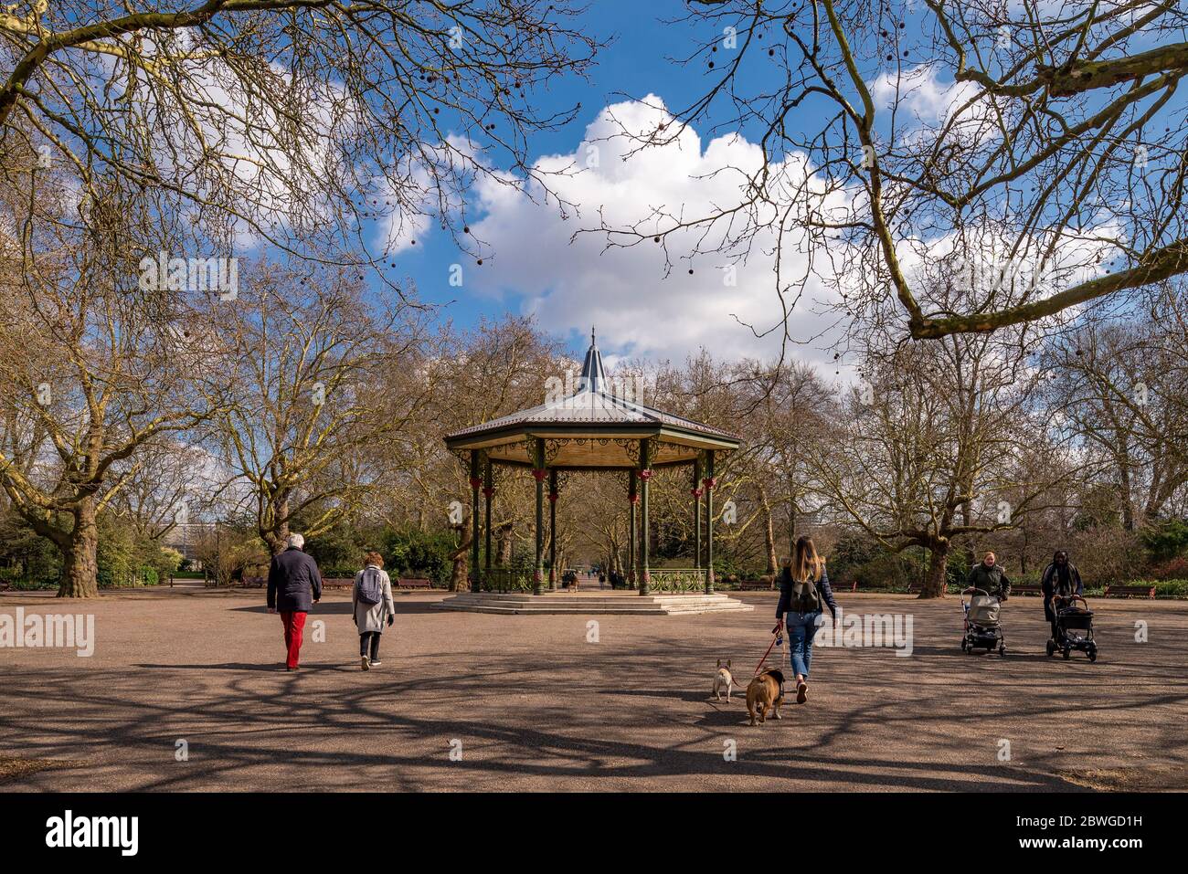 Battersea Park scene busy with dog walkers, couples and parents with bandstand in centre of pathways though the leafy green space Stock Photo