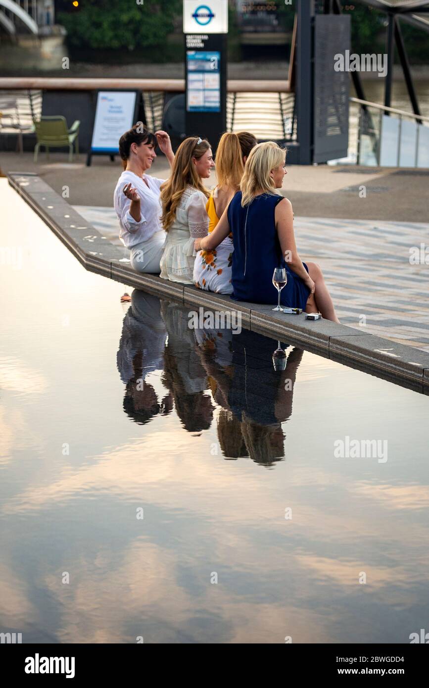 A group of women friends sit beside a water feature in the public space on Riverside Walk next to Battersea Power Station redevelopment,  River Thames Stock Photo