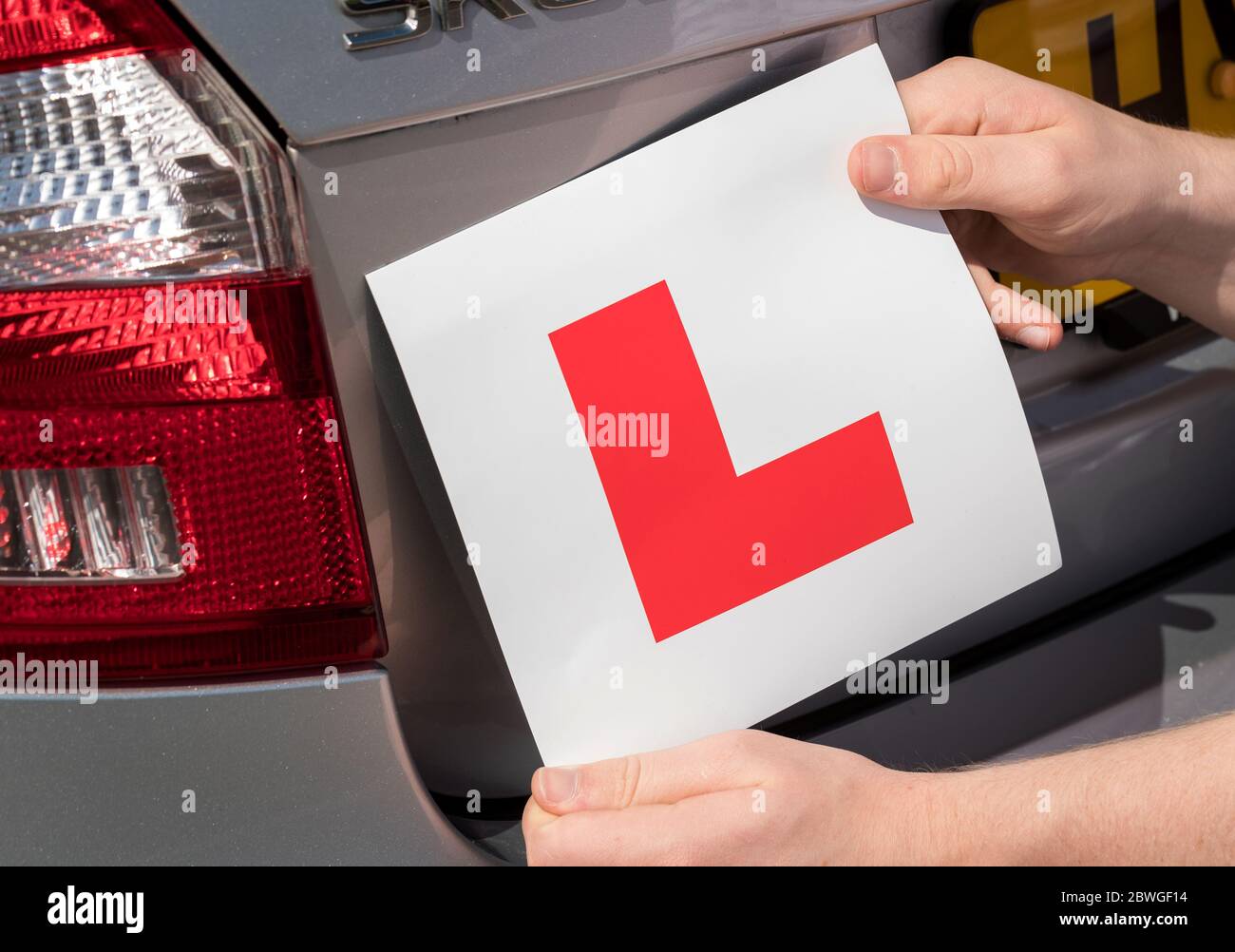 Close up of teenage learner driver adding L plate to his parents car Stock Photo