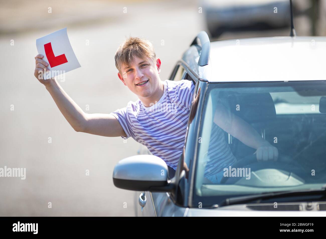 Teenager learner driver celebrating passing his driving test waving his L plates in the air. Stock Photo