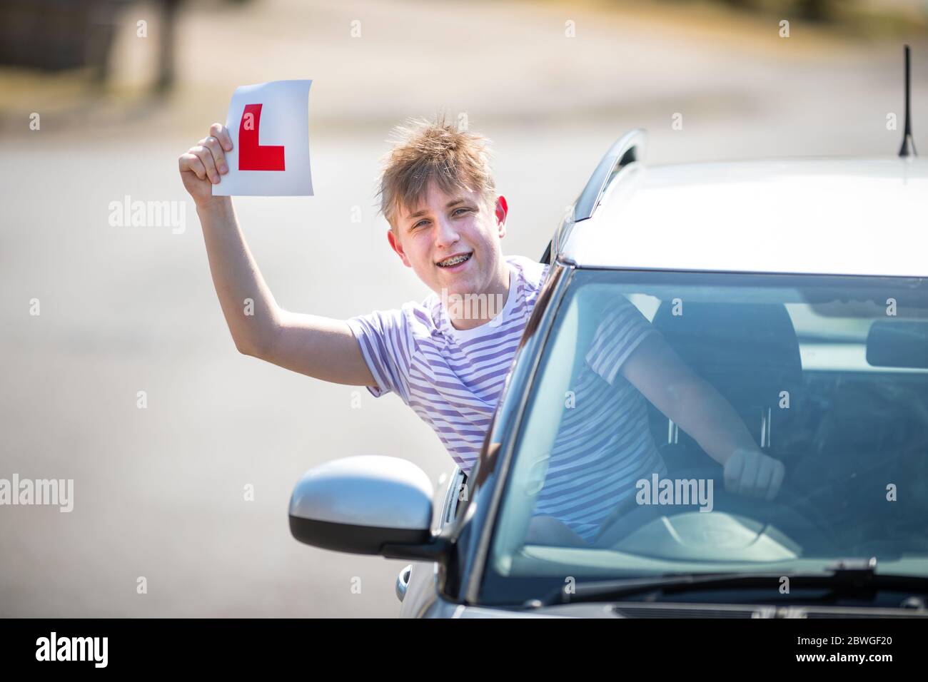 Teenager learner driver celebrating passing his driving test waving his L plates in the air. Stock Photo