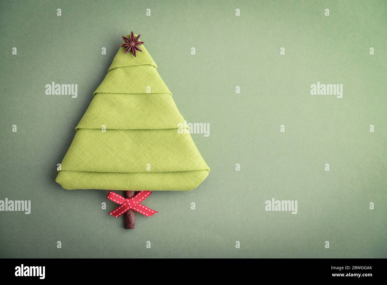Napkin in the shape of a Christmas tree with anise star and cinnamon stick as a  tree trunk on green background, top view Stock Photo