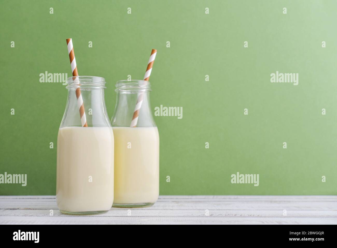 Two bottles with milk and drinking straws on green background Stock Photo