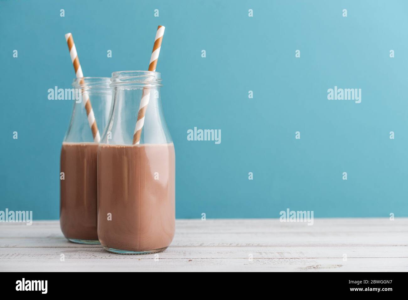 Two bottles chocolate milk with drinking straws on blue background ...