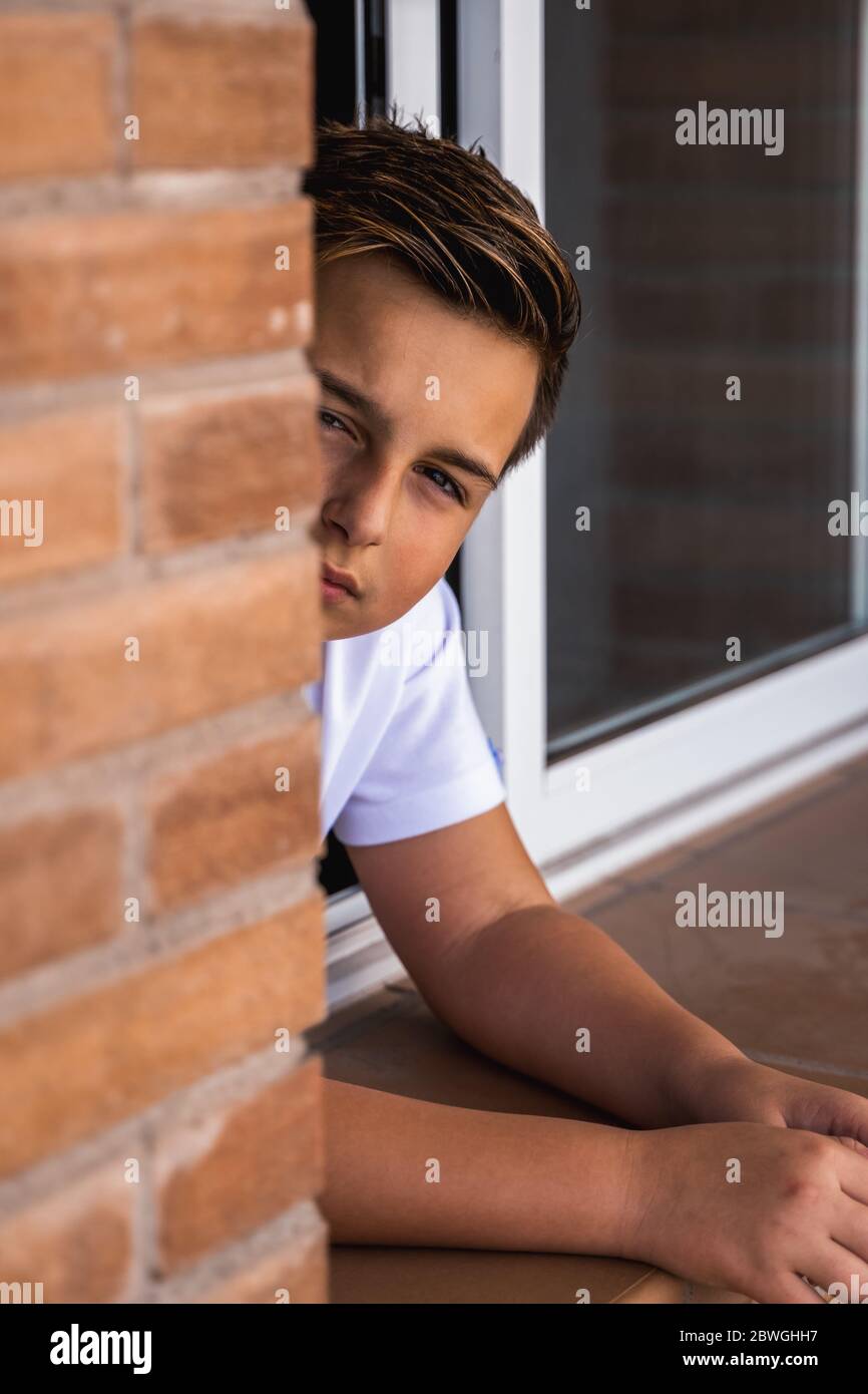 Modern teenager leaning on sill of window in brick house and looking at camera Stock Photo