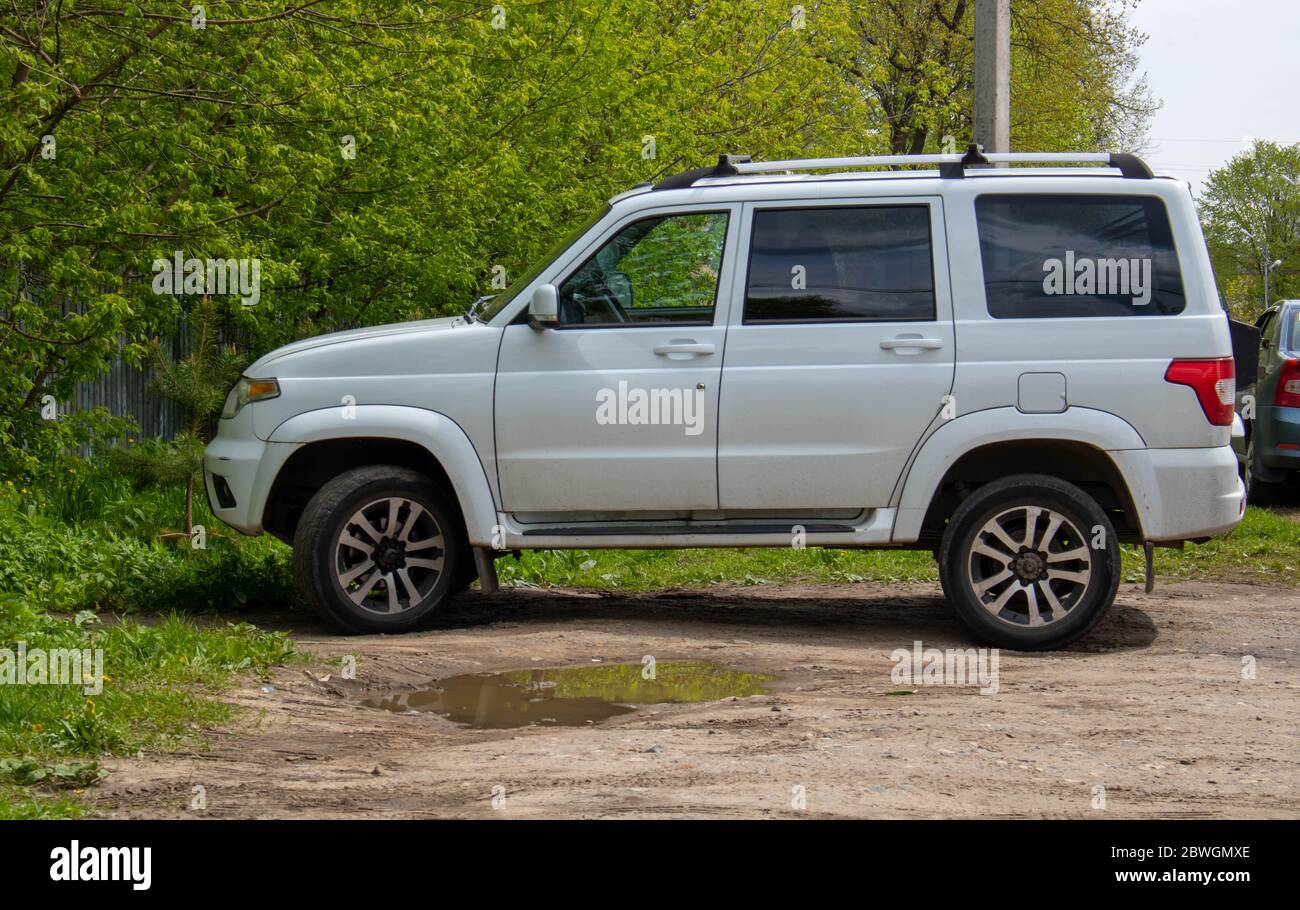 Rybinsk, Russia-may 26, 2020. Side view white UAZ Patriot stands next to the greenery of spring trees. Stock Photo