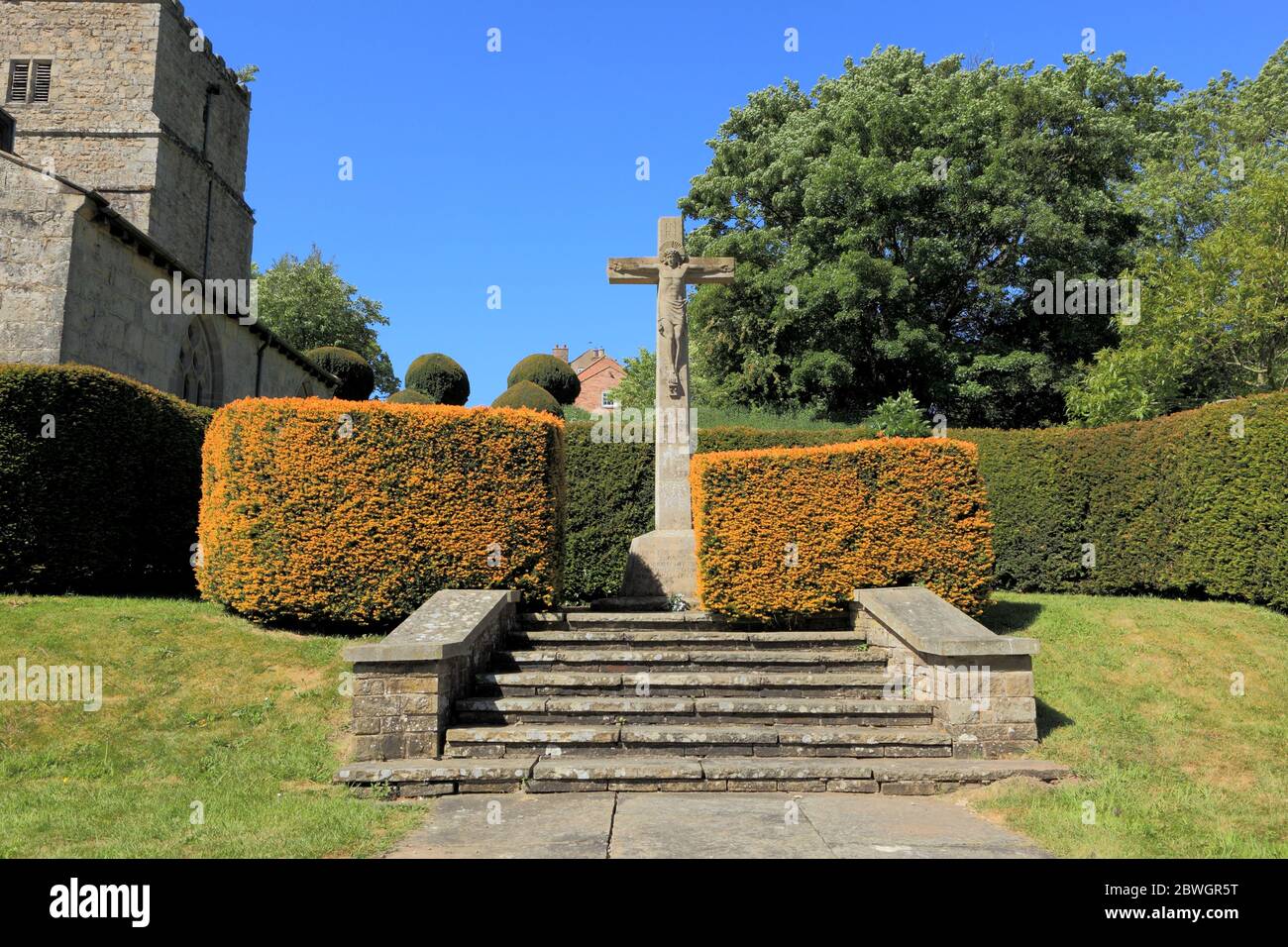 Neatly trimmed hedges around the statue of Christ on the cross in the beautiful churchyard at Kirby Underdale on the Yorkshire wolds in summertime. Stock Photo
