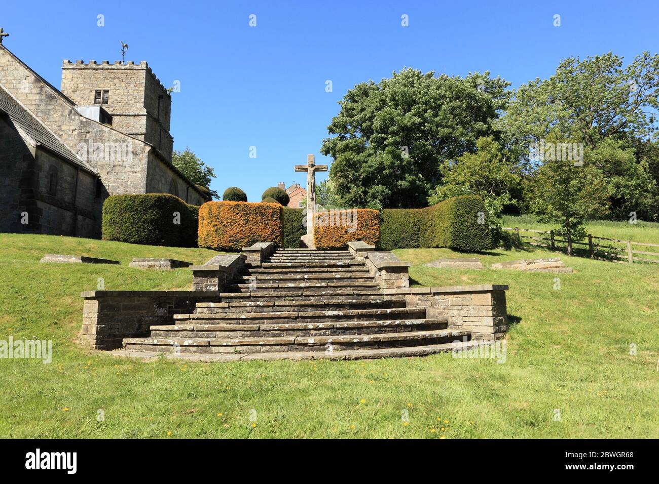 Stone steps leading up to a statue of Christ on the cross in the beautiful churchyard at Kirby Underdale in the Yorkshire wolds in summertime. Stock Photo