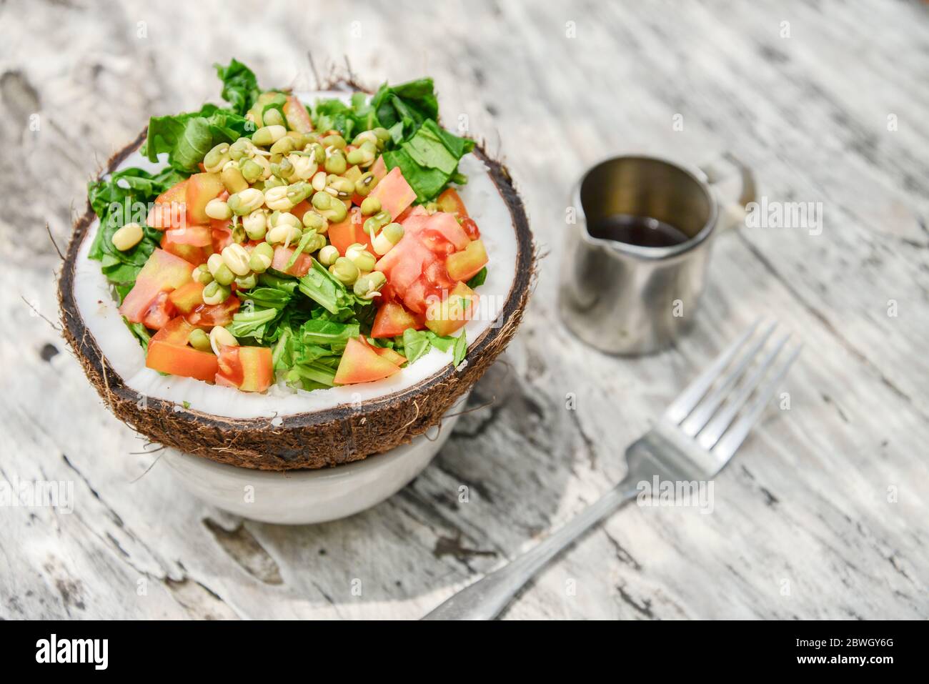 Salad with tomato, greens,  sprouted mung beans and coconut pulp served in half coconut on white wooden background Stock Photo