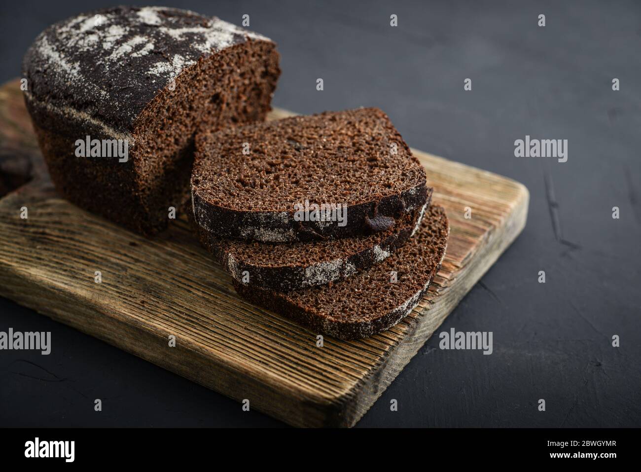 Wholegrain rye bread on a weathered wooden board on dark background Stock Photo