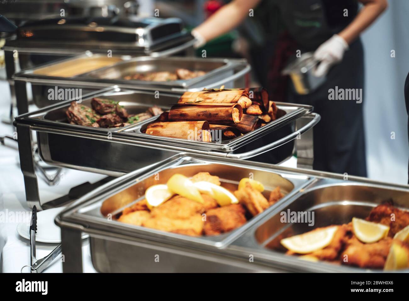 Row of stainless hotel pans on food warmers with various meals. Self