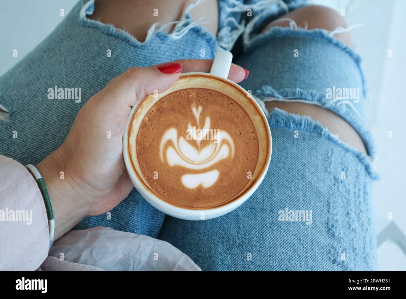 https://c8.alamy.com/comp/2BWH261/female-hand-holds-a-cup-of-cappuccino-on-her-knees-in-a-cafe-top-view-2BWH261.jpg