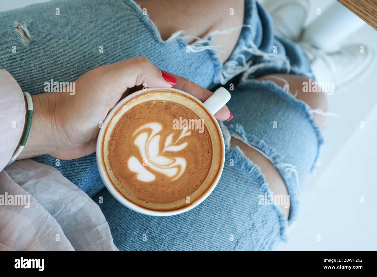 https://c8.alamy.com/comp/2BWH262/female-hand-holds-a-cup-of-cappuccino-on-her-knees-in-a-cafe-top-view-2BWH262.jpg