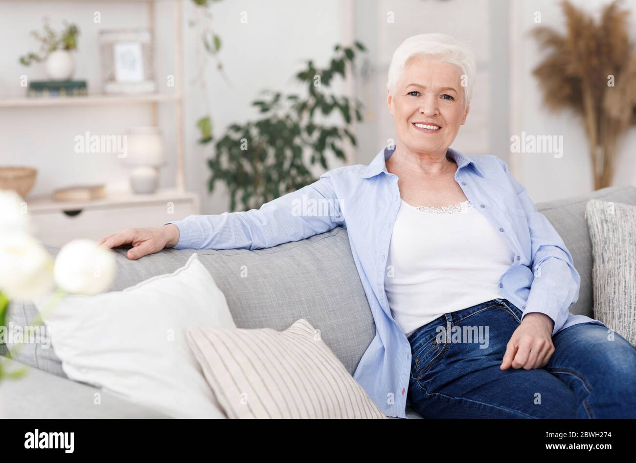 Smiling Elderly Lady Posing On Couch In Living Room At Home Stock Photo