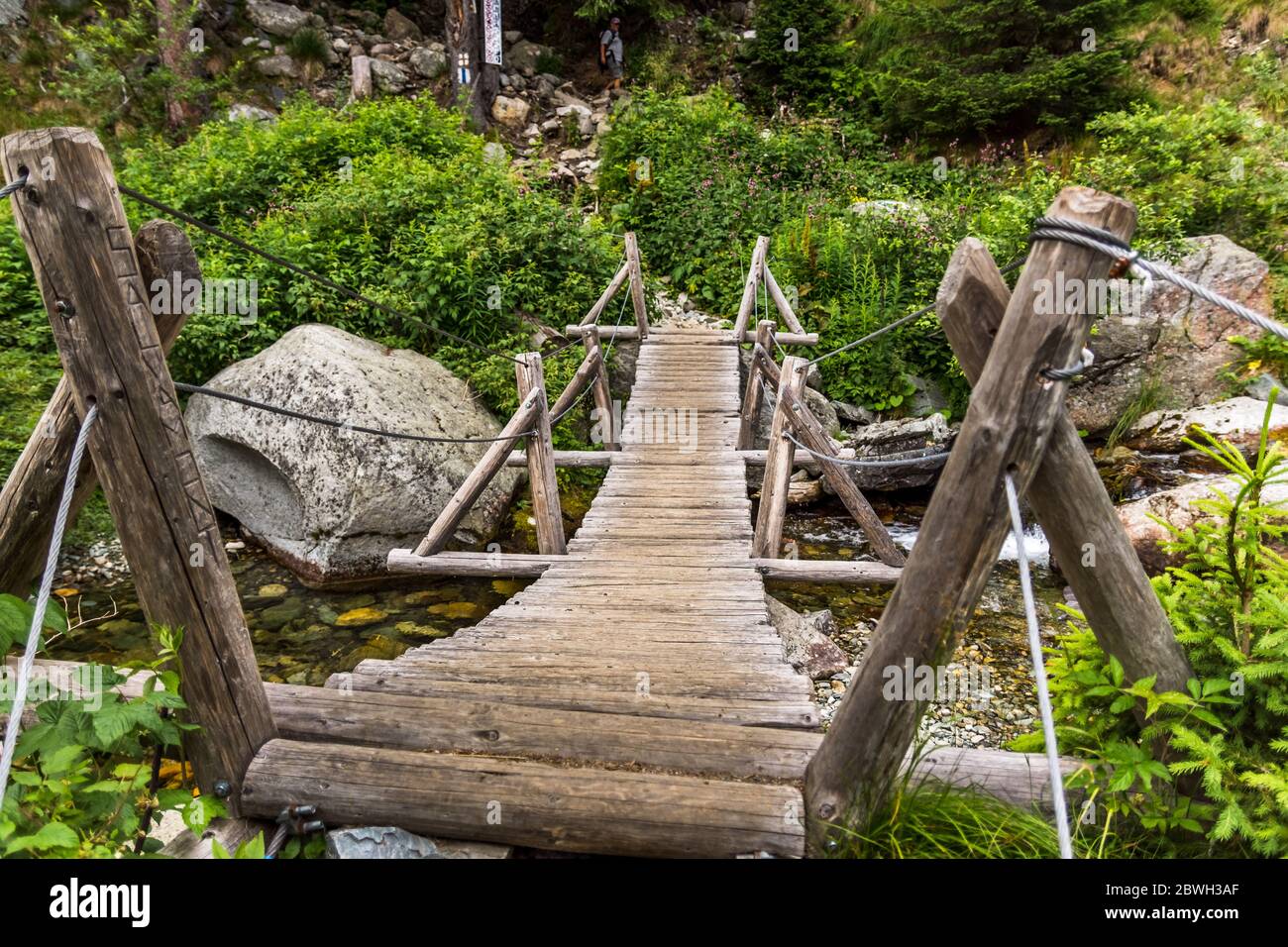 Old wooden bridge crossing over mountain stream in Romanian mountains Stock Photo