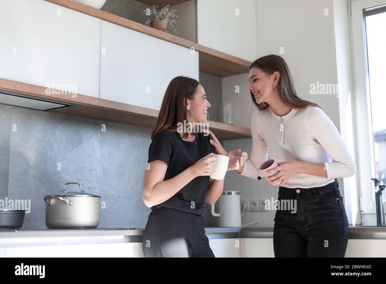 Two young laughing women standing at kitchen and enjoy Stock Photo