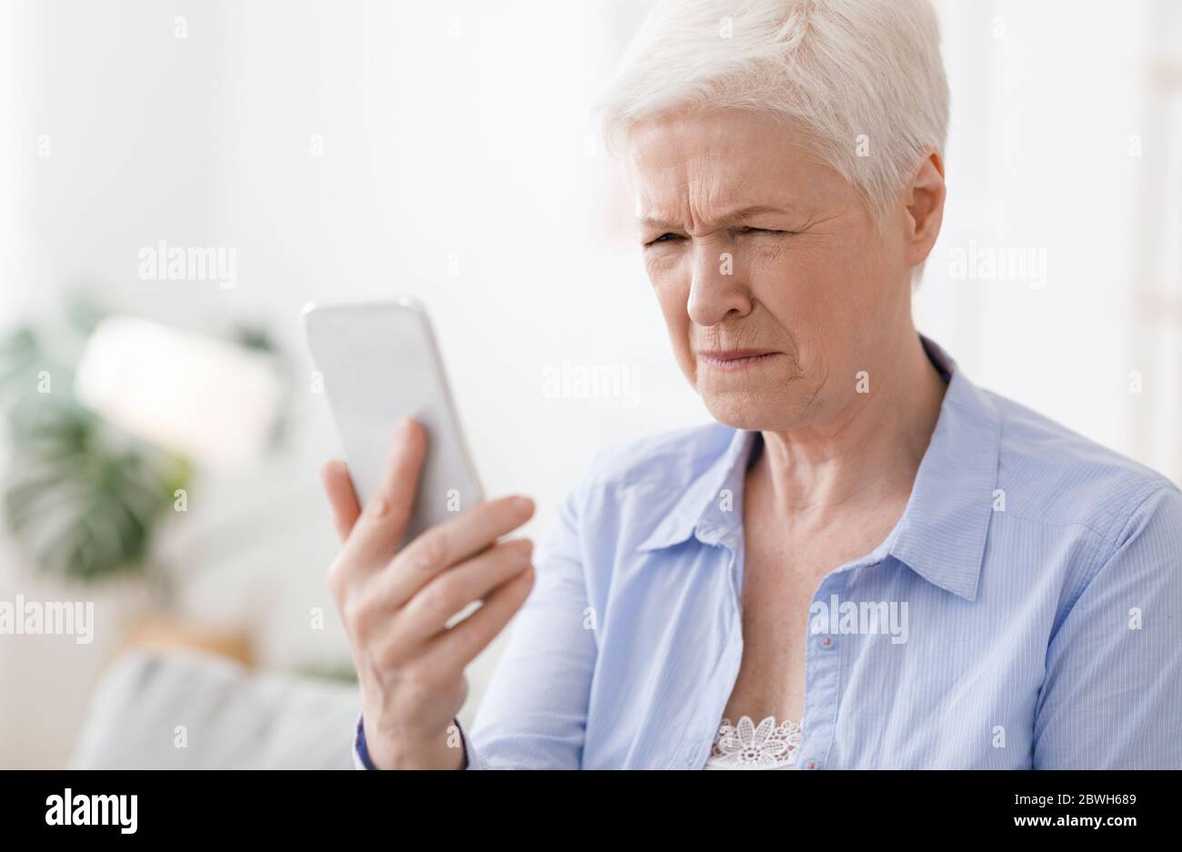 Myopia Concept. Elderly woman squinting while looking at smartphone screen Stock Photo